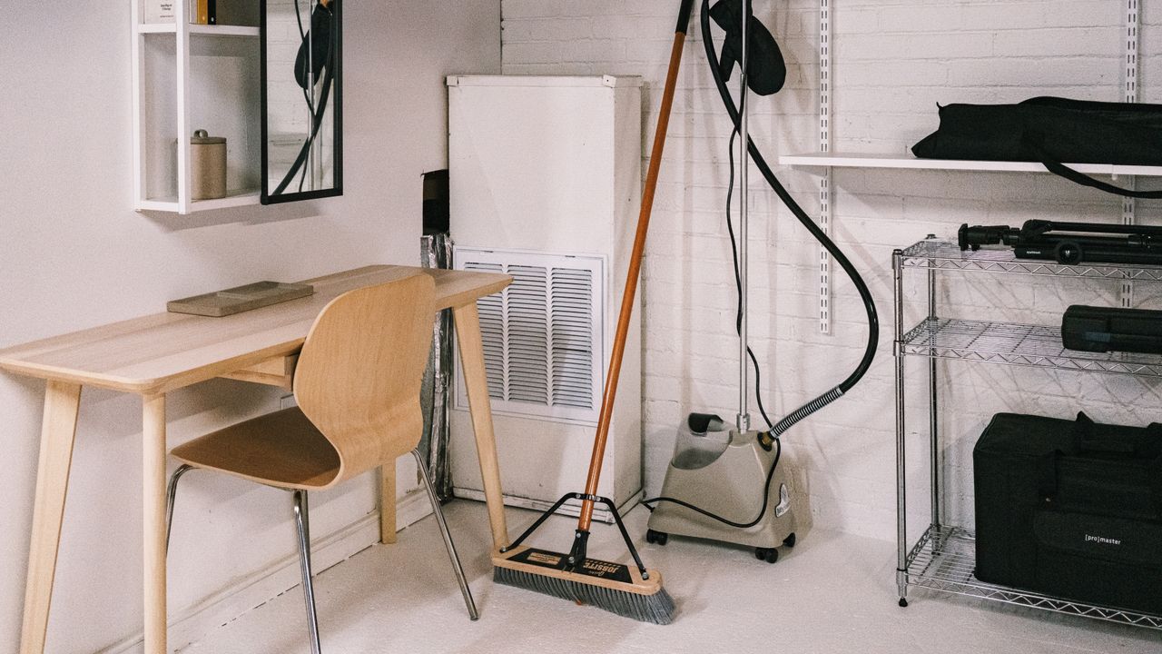 A well-kept home office area with a wooden desk, chair, broom, and cleaning tools.